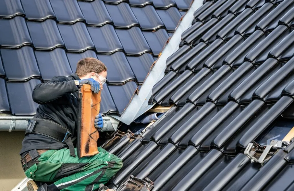 A worker repairing tile-integrated photovoltaic roof shingles