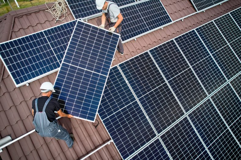 Two workers installing solar panels on the roof of the building