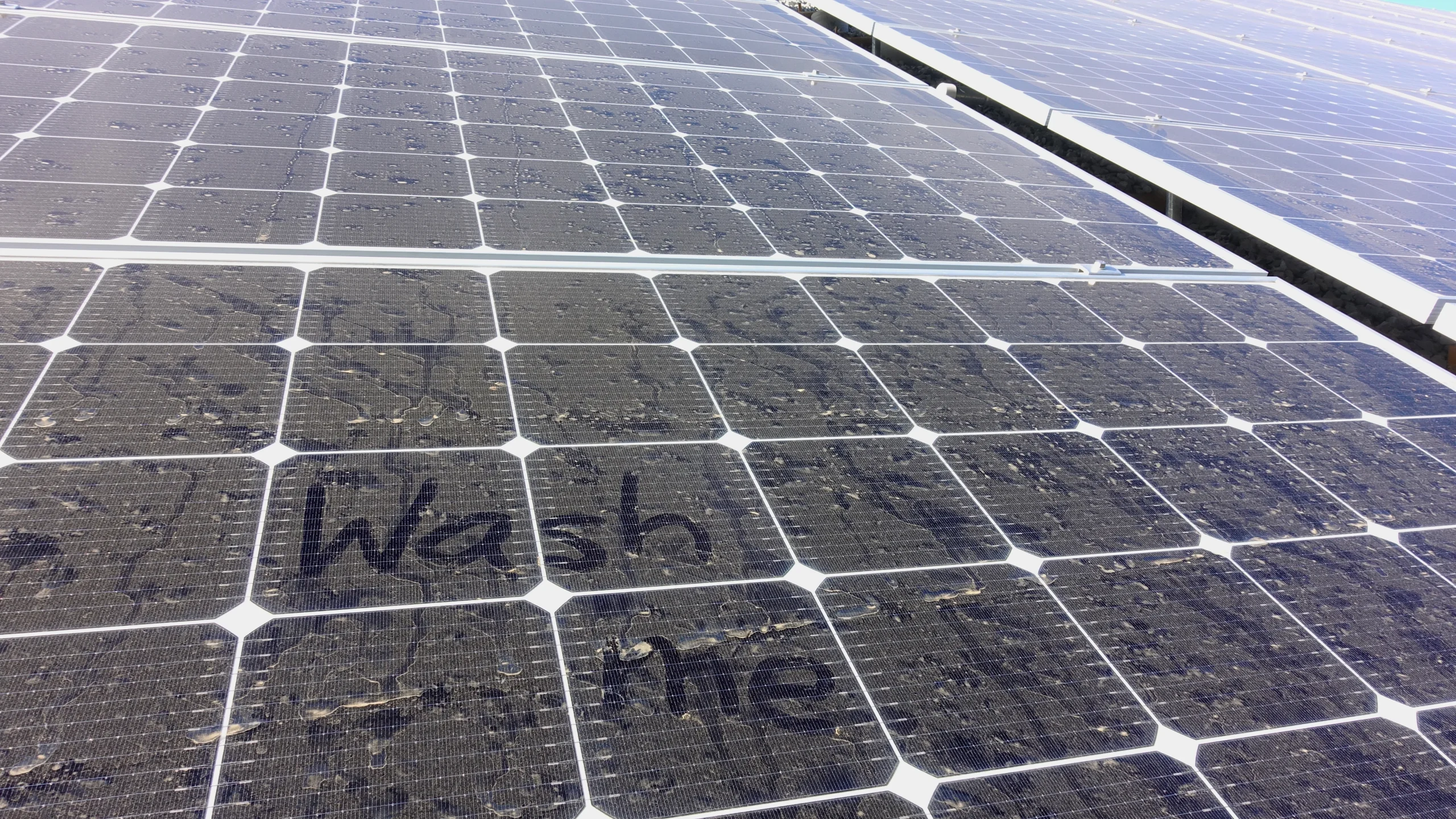 Dusty solar panels that have a phrase "wash me" written on them