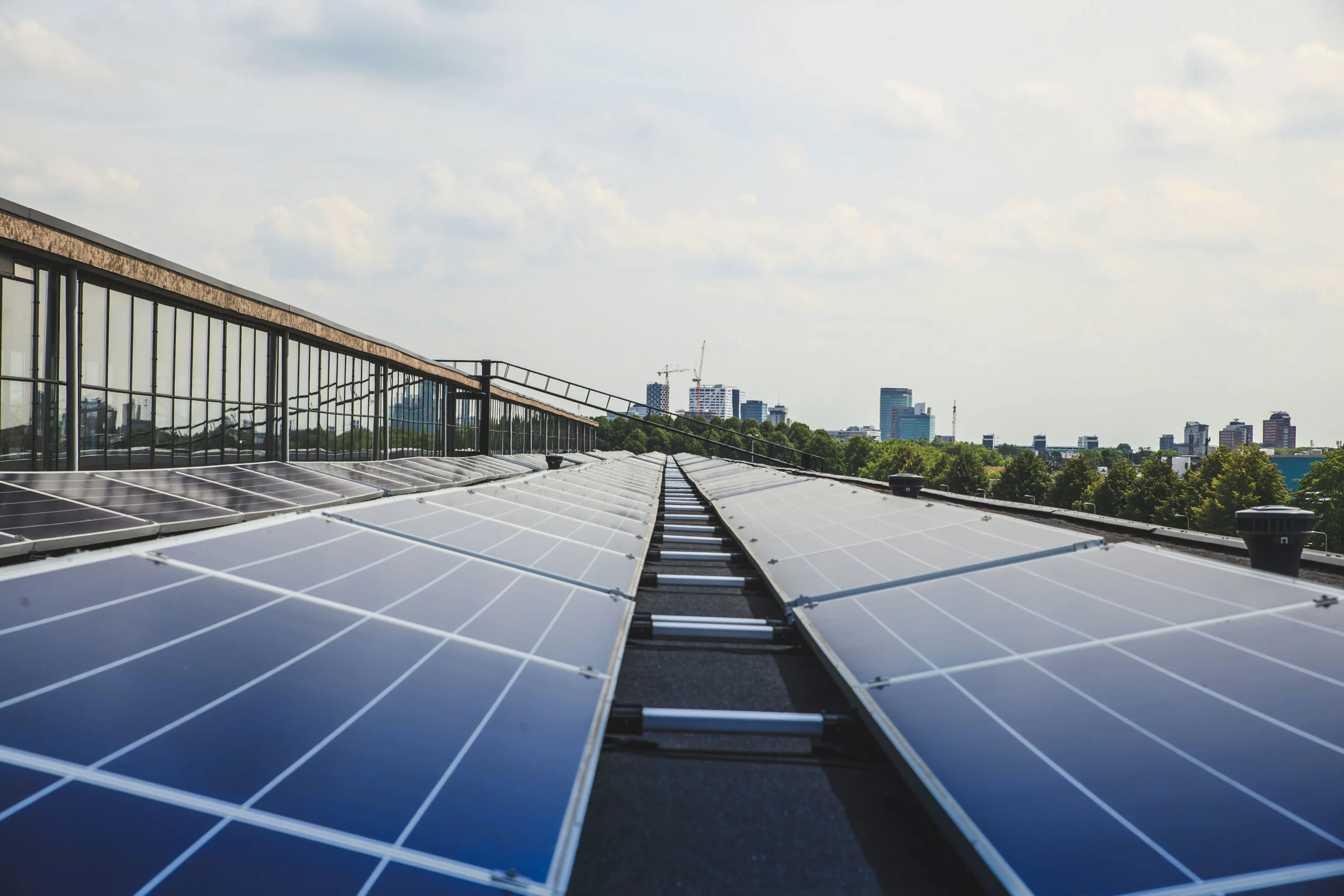 A row of solar panels installed on the roof with a cityscape in the background.