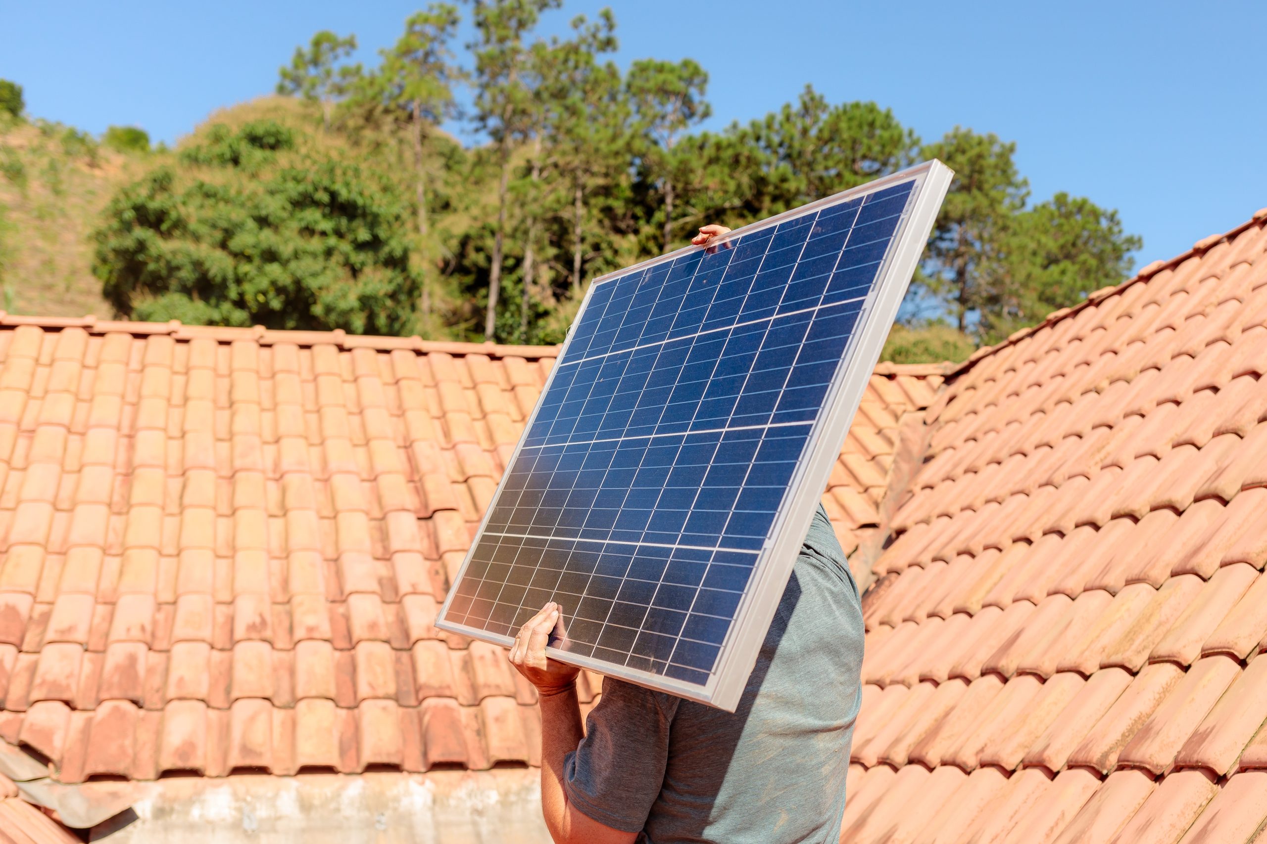 A solar technician carrying a solar panel to install it on the roof of the residential building