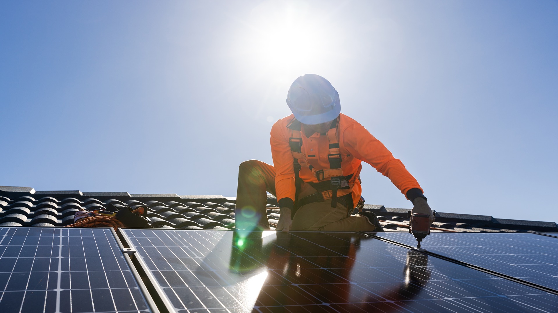 A solar panel technician installing solar panels on a house roof on a sunny day