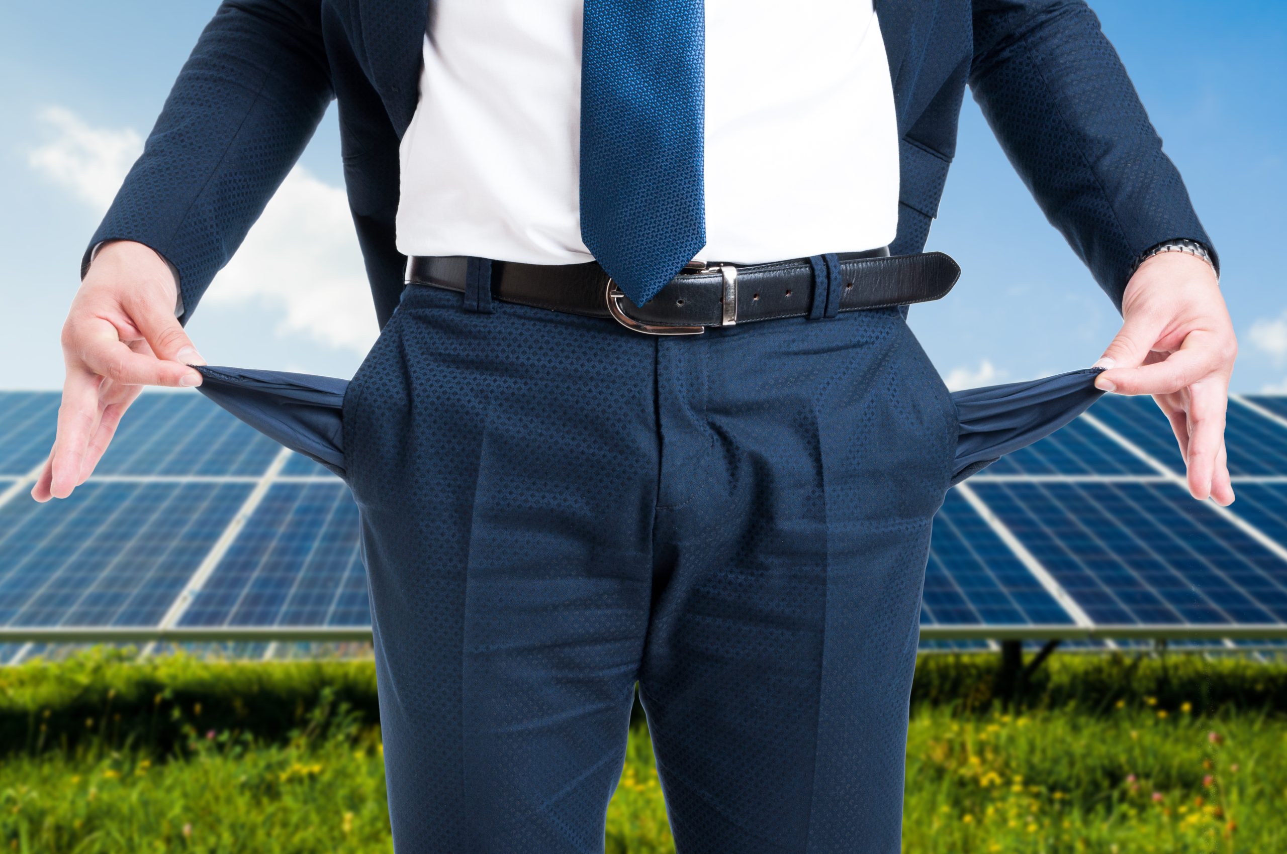 A businessman showing the empty pockets with solar panels in the background, visualizing solar company bankruptcies