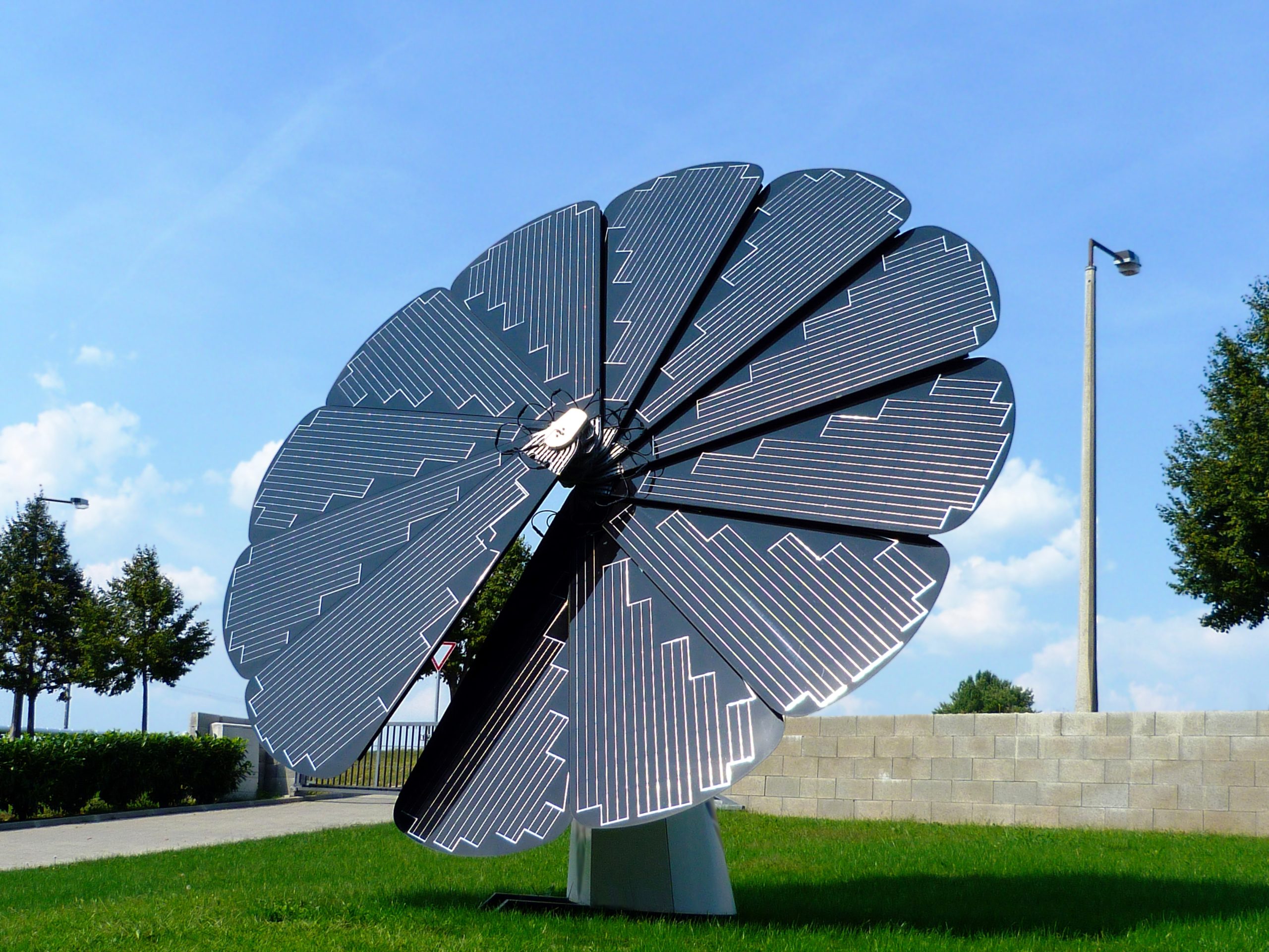 A self-controlled, rotating solar flower system with green grass and trees in the background