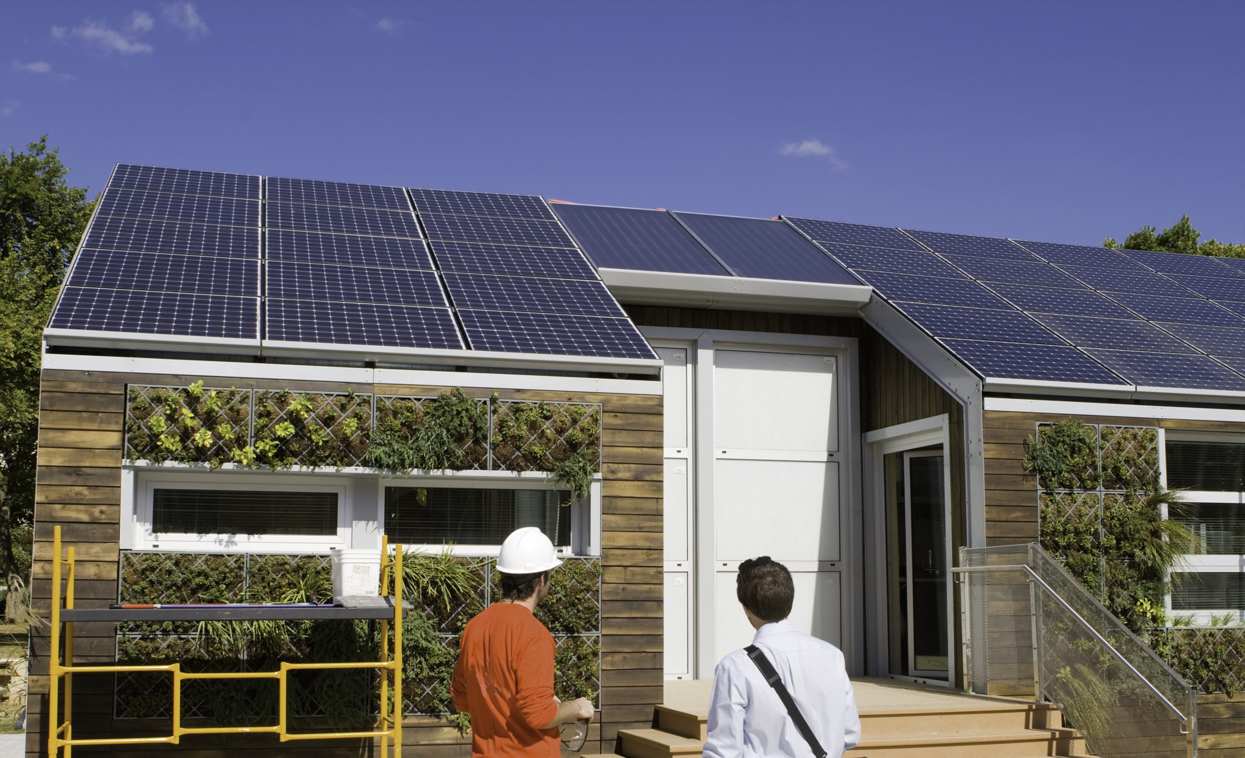 Solar construction workers looking at the on-grid solar system on the roof of the house with plants