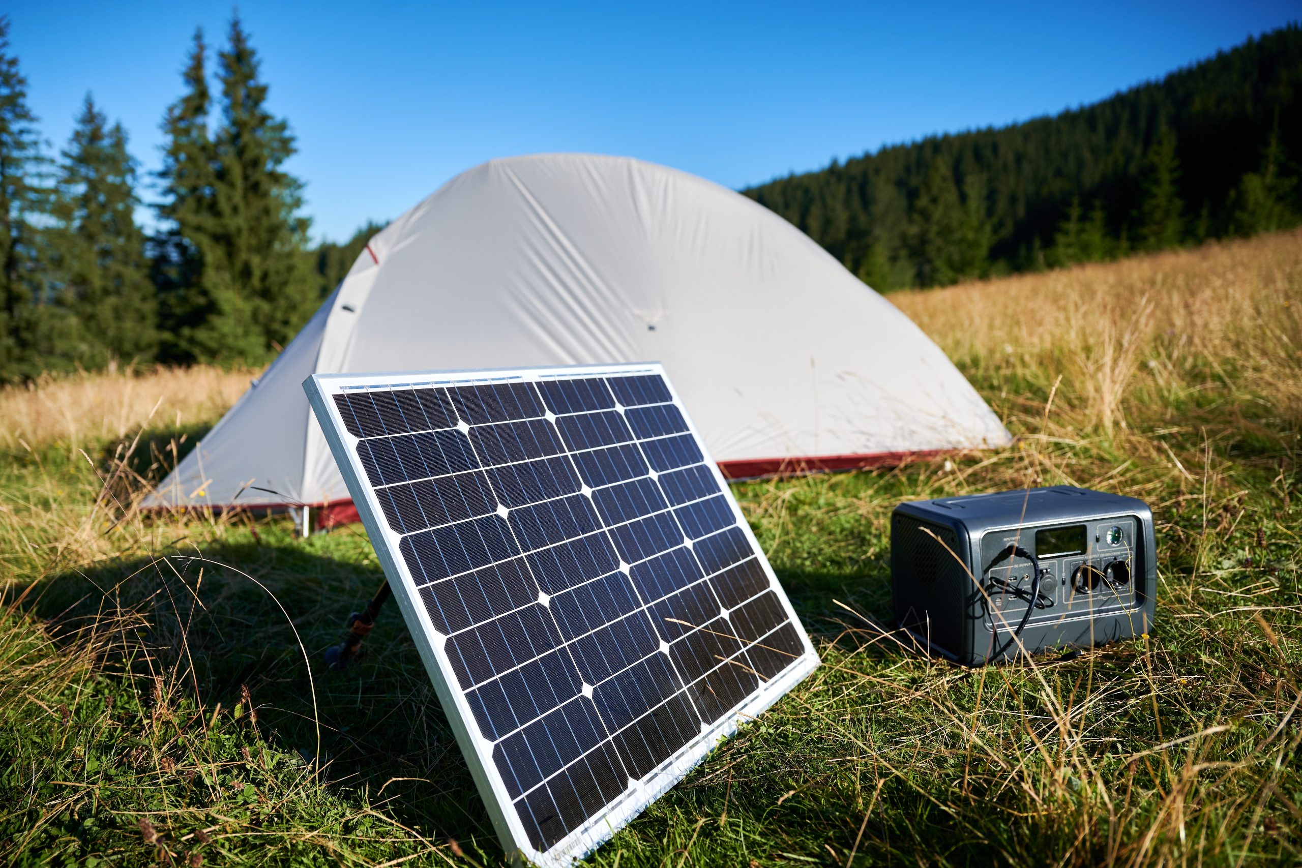 A tourist tent with a solar power generator alongside a solar panel in a grassy field