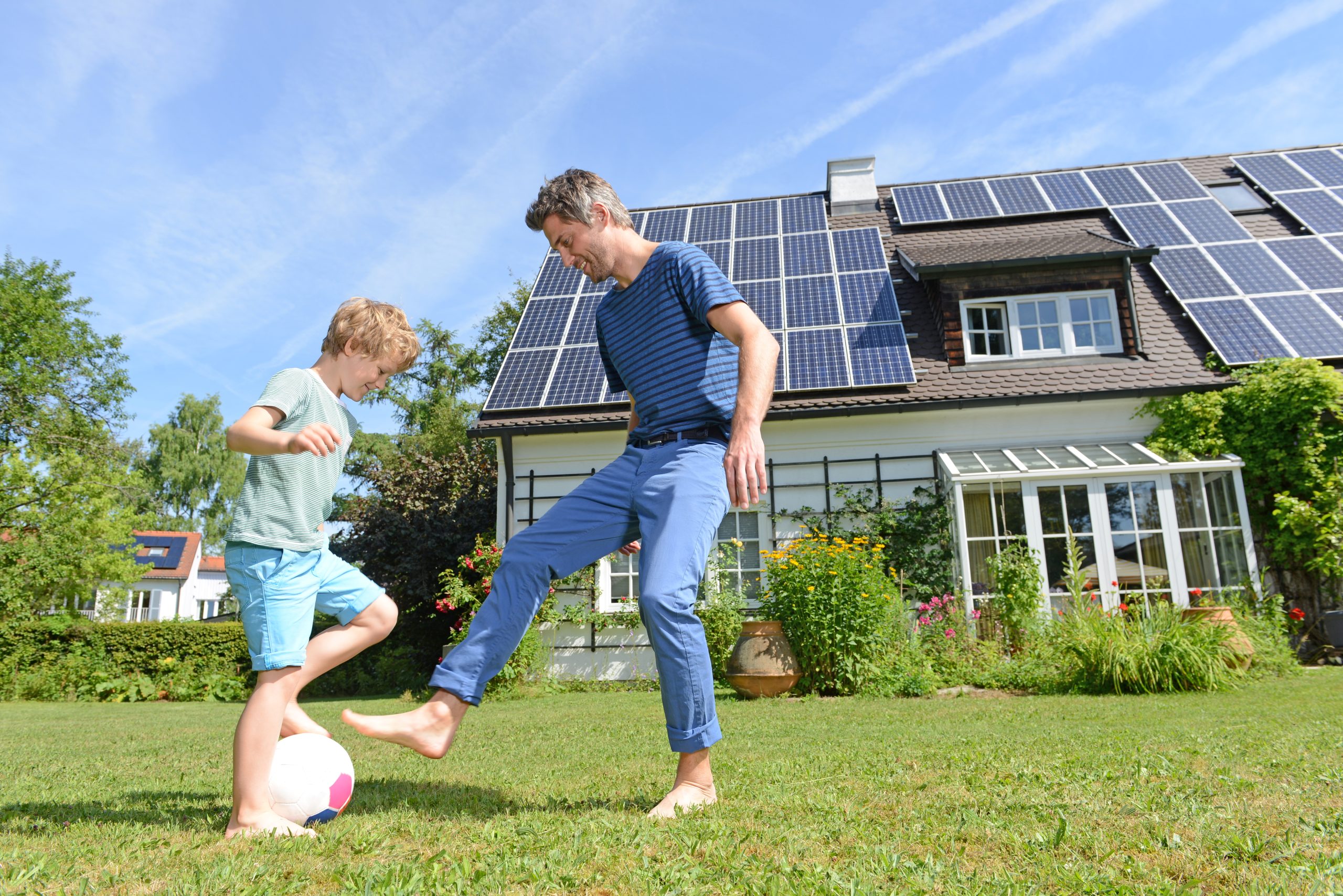 Father and son playing football in front of the house with solar panels installed on the roof