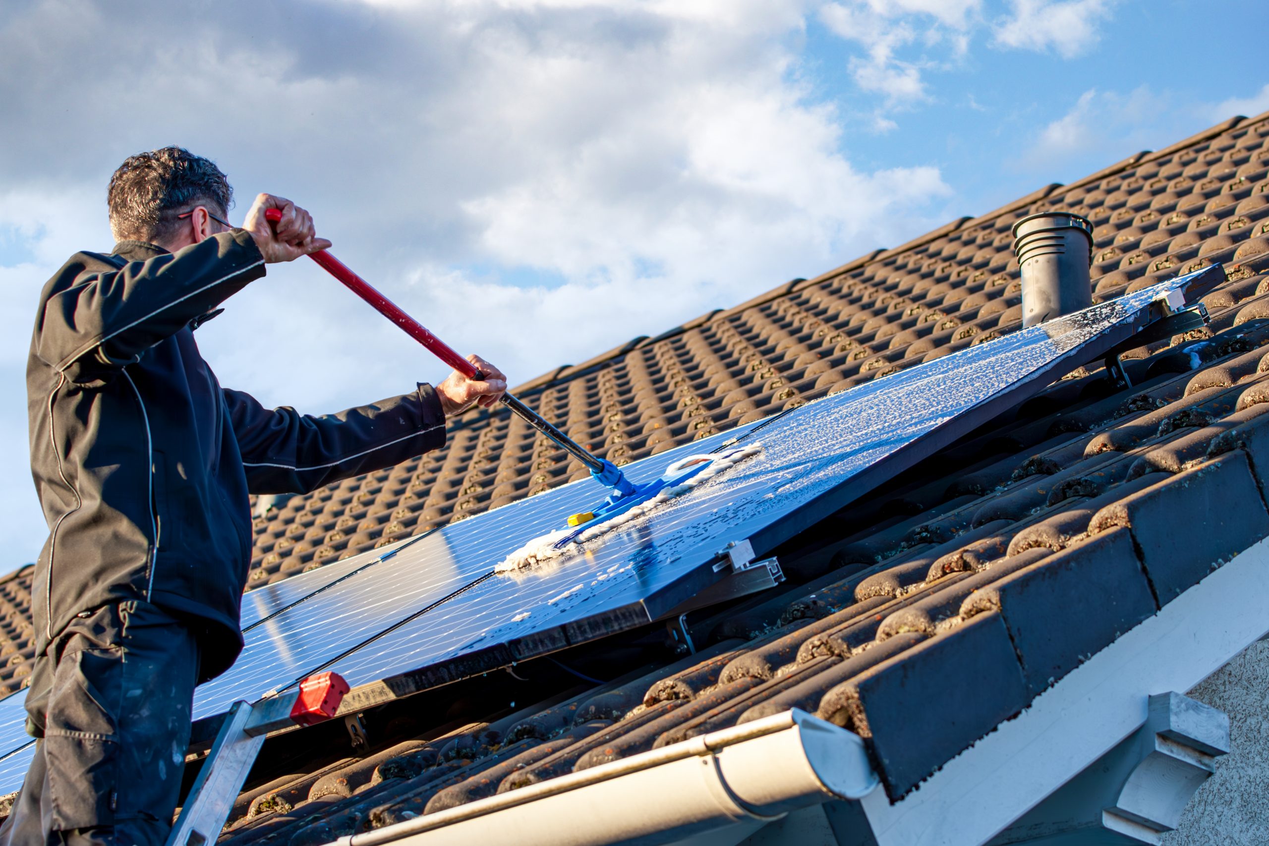 A man cleaning solar panels with a mop on a sunny day, following the DIY solar panel cleaning tips