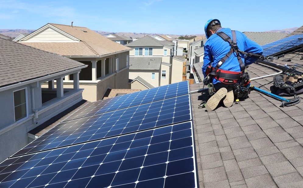 A technician installing solar panels on a residential rooftop in a suburban neighborhood.