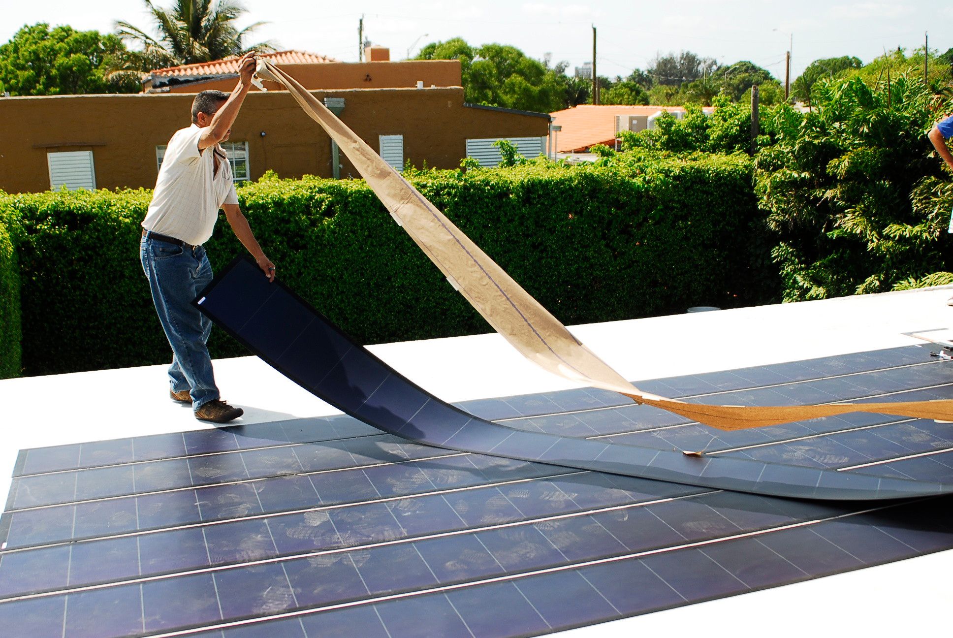 Installer applying lightweight flexible solar panels to a flat roof using adhesive, demonstrating an alternative mounting method without traditional racking