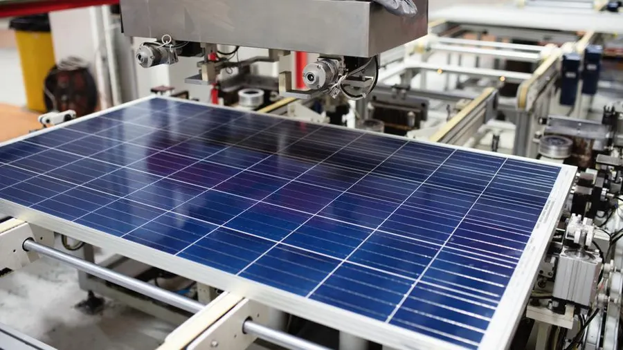 A solar panel being assembled on an automated manufacturing line, with machinery positioning the panel during production.