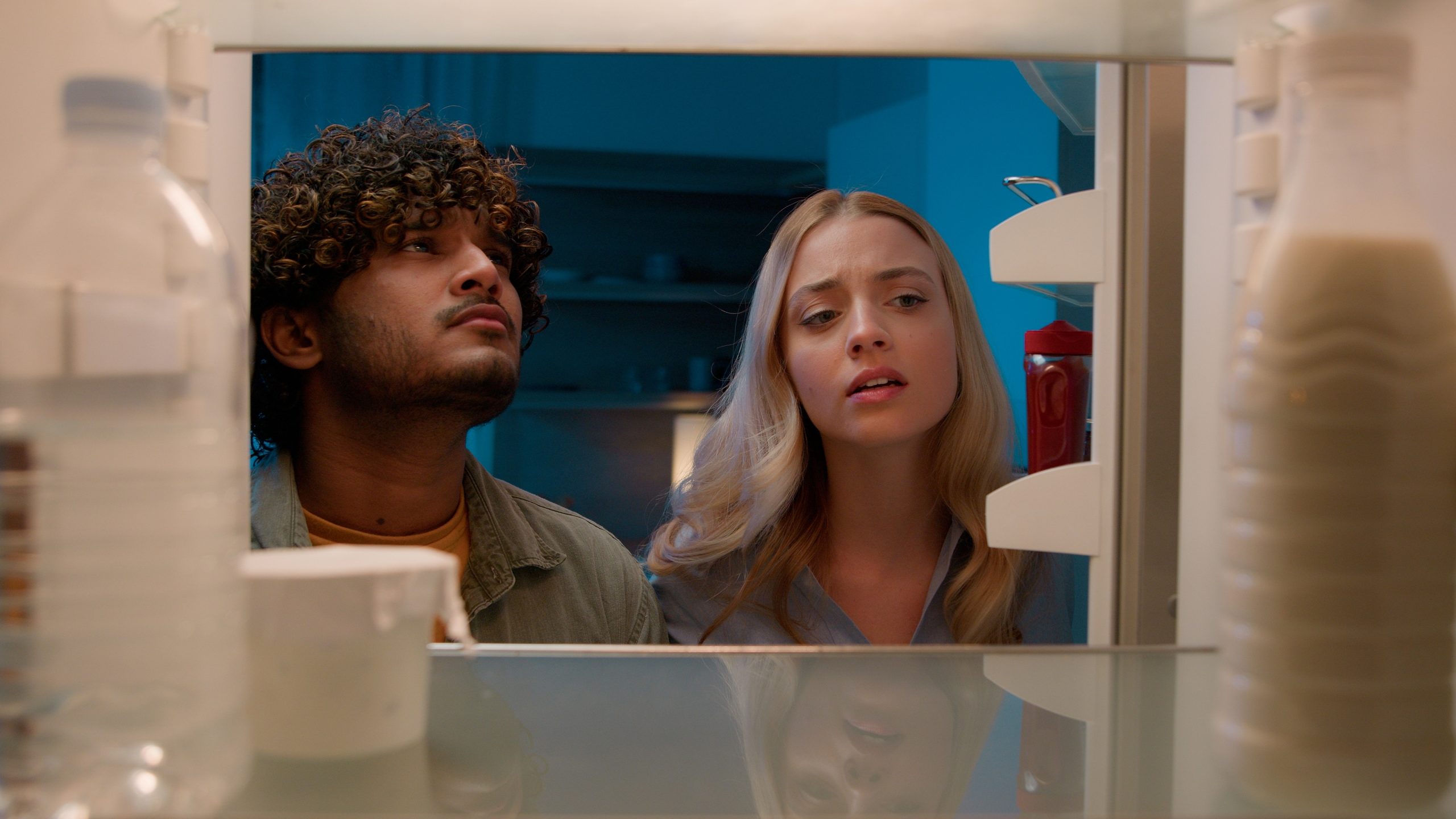 Man and woman looking inside an open refrigerator, checking its contents and energy usage